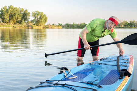 在科罗拉多州北部一个平静的湖上站起来 paddleboard 的高级男性桨手的环境肖像, 夏季风光