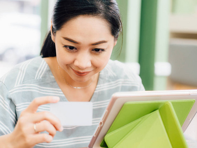 快乐亚洲妇女使用白色样机信用卡在线购物平板电脑