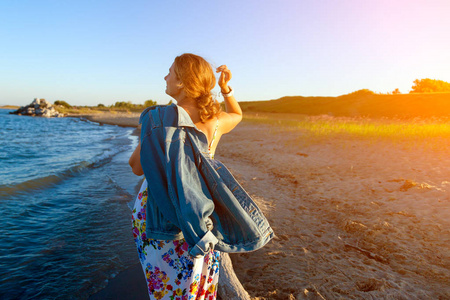 一个开朗的黑发女人在彩色的线和牛仔夹克微笑着, 沿着海滩漫步, 享受灿烂的阳光在夏天的一天