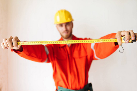 关闭工头在橙色工作衣服和黄色安全帽持有测量磁带的白色背景