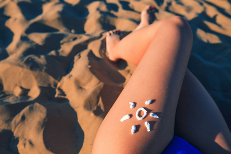 皮肤护理的概念。在沙子背景上女孩腿特写的太阳霜