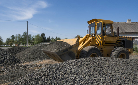 在公路建设工程中, 黄色装载机与碎石一起移动。道路上的石头。卸石