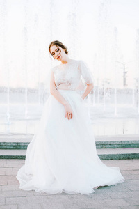 快乐的年轻新娘在流动的白色礼服享受自己的户外和在喷泉附近跳舞