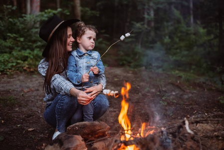 母亲和女儿在森林的篝火上烤棉花糖糖果。春季或秋季露营