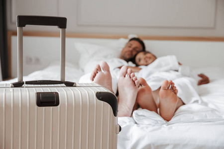 模糊的形象, 美丽的夫妇男子和妇女在白色浴衣躺在床上, 并在酒店房间与大行李在前台。度假理念