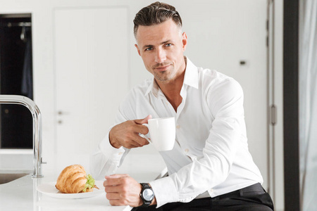 英俊的男子穿着正式的衣服吃早饭, 而坐在厨房