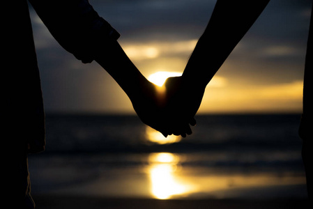 爱的象征。剪影夫妇人和妇女手一起举行在海和天空背景在日落期间为友谊天, 爱和情人节概念