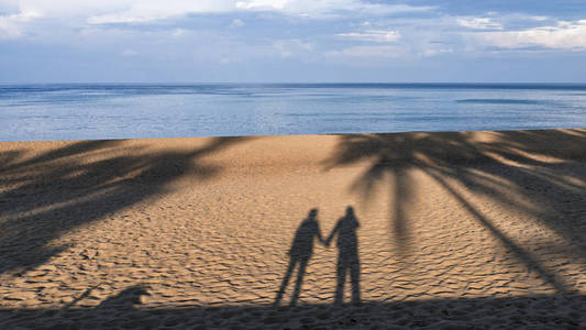 一个男人和女人的影子站在沙滩上牵着手的沙子.爱情理念照片