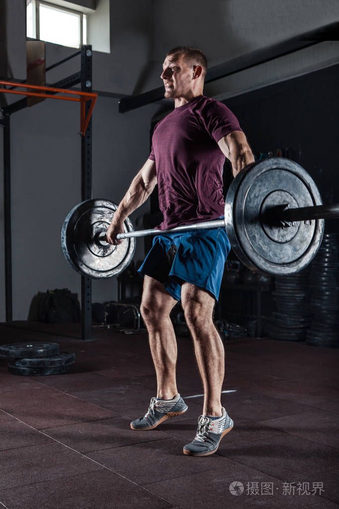 年轻运动员在健身房里用沉重的杠铃在头顶上蹲着.