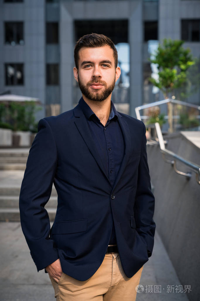 自信的年轻 businessmanin 在城里站着穿蓝色西装.