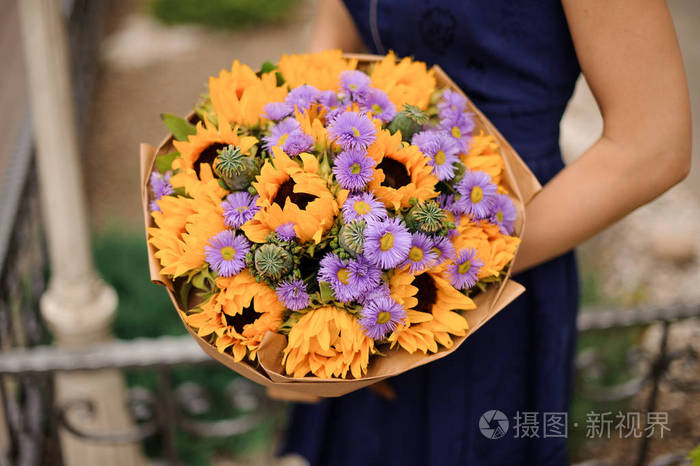女孩在蓝色礼服在她的手拿着一束美丽的向日葵和9月花在礼品纸上