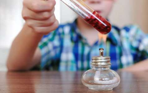 特写男孩手用红色液体在燃烧的酒精灯上加热试管照片