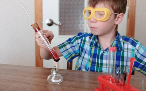 室内化学实验.男孩用红色液体在燃烧的酒精灯上加热试管.液体沸腾照片