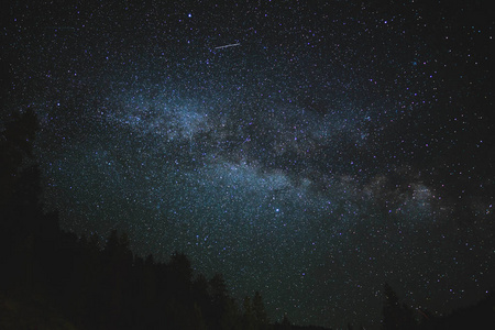 一颗流星穿过银河系越过遥远的森林。夏日夜空中的新月