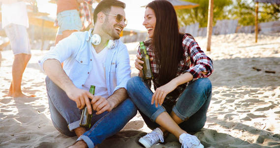 快乐的年轻夫妇喝啤酒, 并在海滩上的乐趣在日落期间