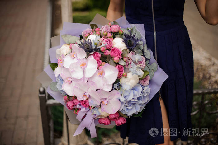 女孩在蓝色礼服在她的手拿着一束柔和的粉红色和紫罗兰色的花在公园的