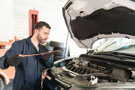 中成年男性工程师在车间日常维护中检查汽车发动机油位