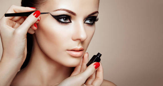 化妆师应用眼影。美丽的女人化妆眼与黑色班轮。时尚化妆箭。红指甲完美肌肤