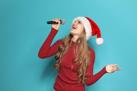 年轻妇女在圣诞老人唱歌入话筒在颜色背景。圣诞音乐