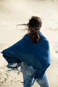 黑发妇女在蓝色布站立在荒凉的风的风景。后视图