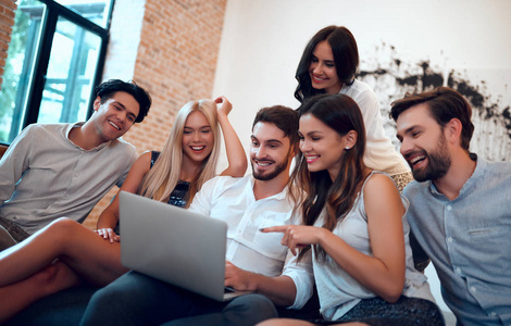 坐在沙发上与笔记本电脑在大公司的密友让大家一起开心的小姐妹年轻