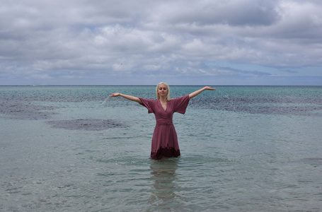 漂亮的金发女孩的肖像穿着紫色的礼服, 摆在美丽的海洋景观照片