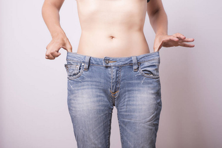 女性身体的拍摄显示节食结果。年轻女子站在旧牛仔裤后体重下降