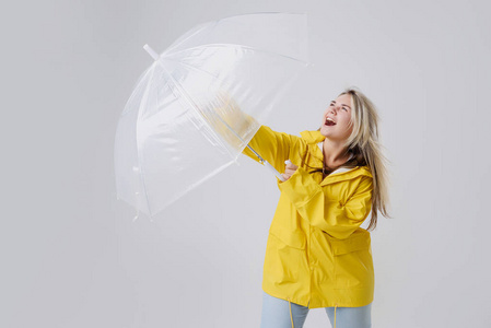 穿着黄色雨衣的金发女郎手持透明雨伞检查天气是否下雨。抵御风雨和飓风