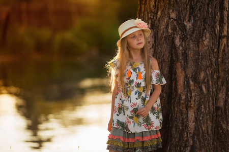 在日落的湖面上戴着帽子的可爱漂亮女孩的肖像