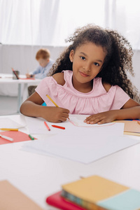 在餐桌上用纸和铅笔微笑的非洲裔美国人孩子的选择焦点在教室里画画