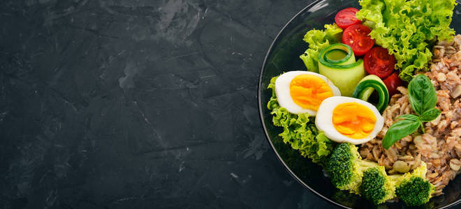 燕麦片配鸡肉蛋, 樱桃西红柿和蔬菜。健康食品。在一个黑色的石桌上。顶部视图。文本的可用空间