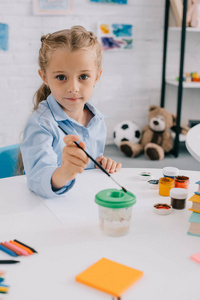 可爱的孩子的肖像坐在桌子与油漆和油漆刷