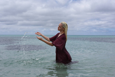 漂亮的金发女孩的肖像穿着紫色的礼服, 摆在美丽的海洋景观照片