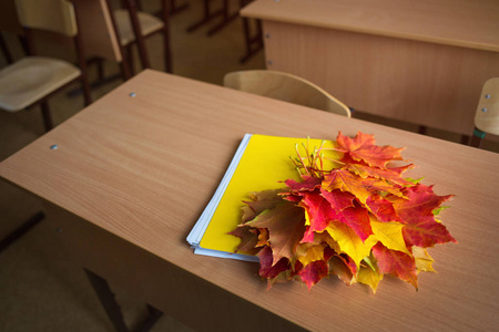 学校教室在模糊背景下没有年轻的学生。桌上放着秋天枫叶的笔记本和花束。理念 回到学校, 教师节