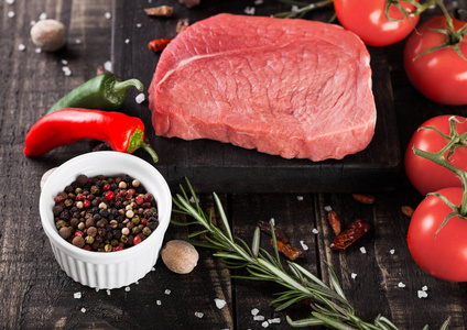 新鲜生牛排肉在木制厨房板用蕃茄和胡椒