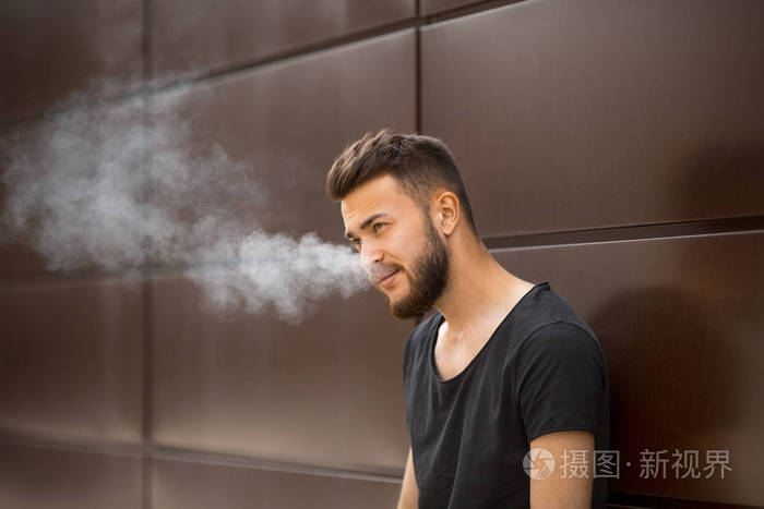 春天, 一个穿着黑色 t恤衫的年轻英俊的白胡子男子在街上抽烟.特写