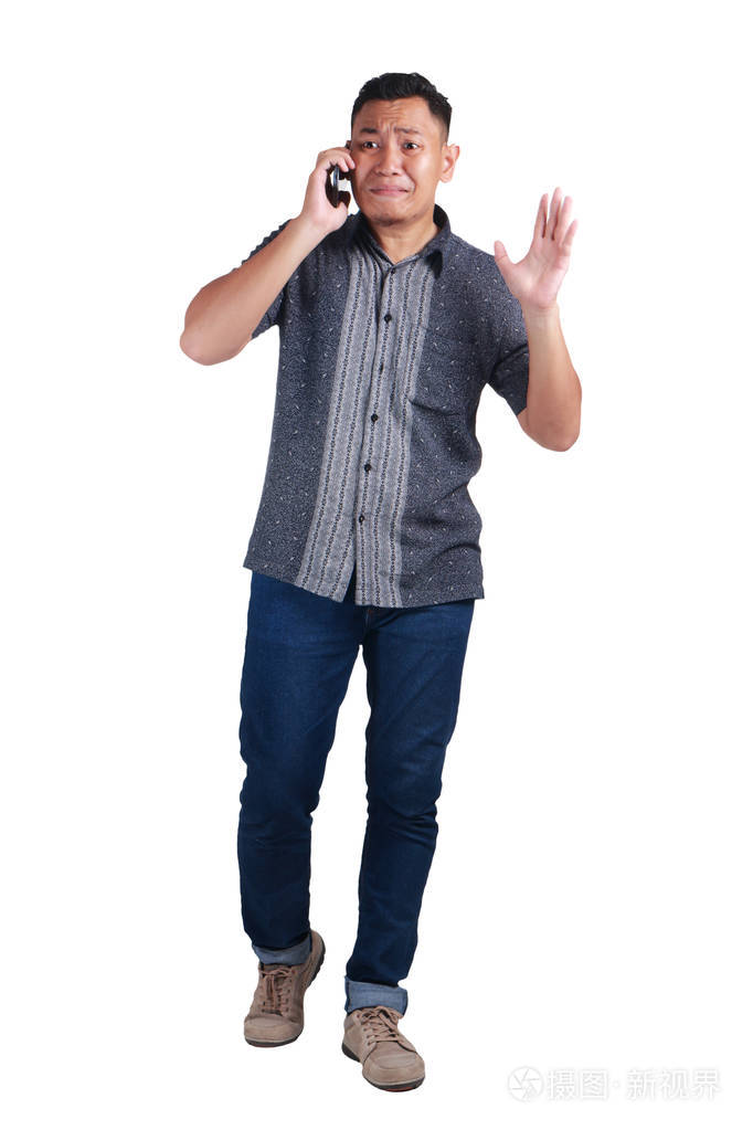 年轻的亚裔男子身穿蓝色牛仔裤和蜡染衫在电话中交谈, 哭着, 神情焦急