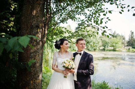 新婚夫妇在他们的婚礼当天在湖边或池塘旁边摆着一棵树。