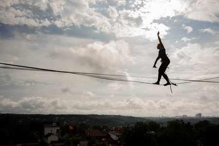 年轻的金发女郎走在 slackline 的绳子上, 在晴朗的蓝天背景下