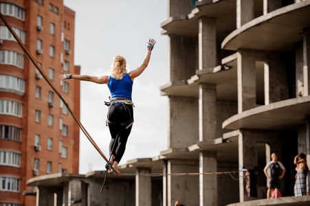 后视图金发女郎走在 slackline 的绳子, 她的朋友在未完工的建筑部分