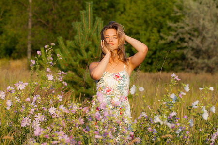 美丽的年轻女子站在田野, 绿草和花朵。户外享受大自然。健康微笑的女孩站在高高的草丛中