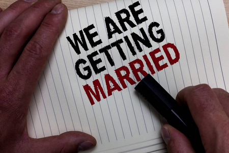 文字写作我们要结婚了。订婚婚礼准备的商业概念爱情侣的手抓住黑色标记与一些黑色和红色的文本在白色页面上