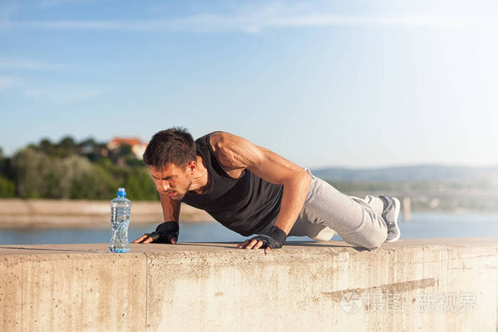 年轻的健身男子在阳光明媚的夏天在户外做俯卧撑.