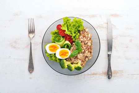 燕麦片配鸡肉蛋, 樱桃西红柿和蔬菜。健康食品。在一个白色的木桌上。顶部视图。文本的可用空间