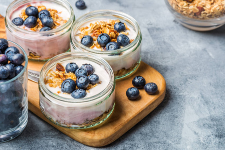 新鲜天然酸奶与自制燕麦片和蓝莓在灰底玻璃罐中的早餐