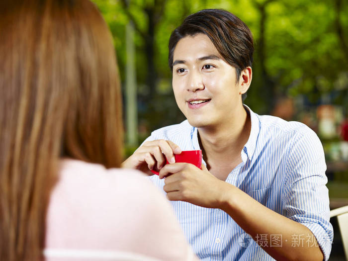年轻的亚裔情侣坐在餐桌外聊天面对面交谈