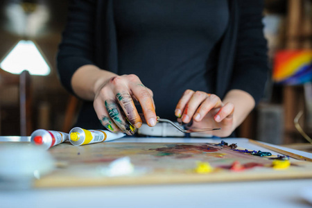 在艺术工作室里, 用不同的颜料和画笔在调色板上关闭女艺术家的脏手