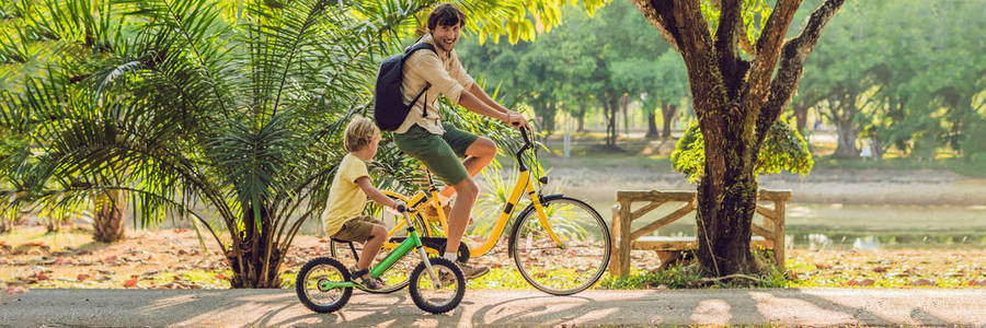 幸福的家庭是骑自行车户外和微笑。父亲骑自行车, 儿子 balancebike。横幅, 长格式