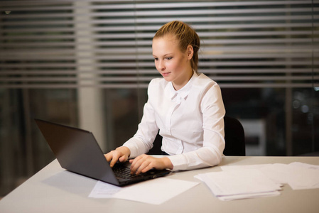 年轻女孩女商人在休闲服装, 坐在桌子旁仔细看文件, 在电脑上工作