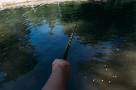 一个人在水上拿着一个绿色的鱼竿, 鱼, 钓到鱼。手持钓竿的人手特写镜头在前景上